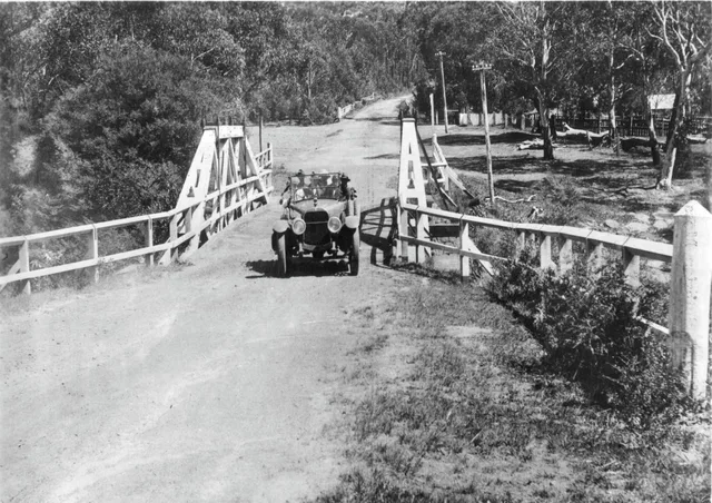 An early motor car crossing a timber road bridge at Fitzroy Falls, dated to the 1920s in the Society caption.