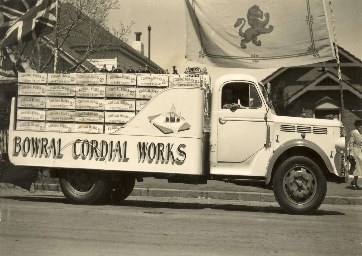 Bowral Cordial Works delivery truck decorated with flags and crates.