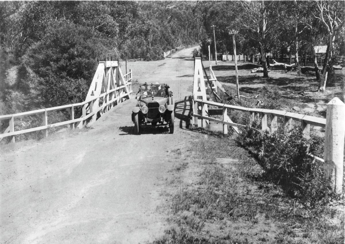 An early motor car crossing a timber road bridge at Fitzroy Falls, dated to the 1920s in the Society caption.